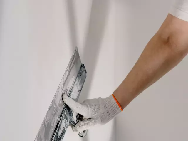 A gloved hand plastering a wall during repairs